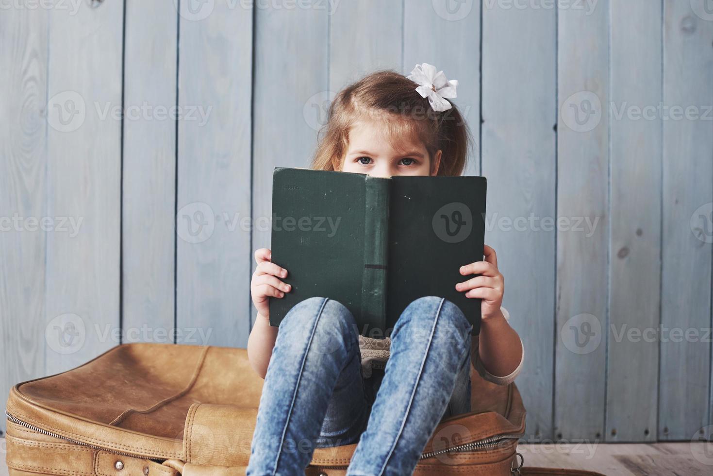 listo para grandes viajes. niña feliz leyendo un libro interesante con un maletín grande. concepto de libertad e imaginación foto