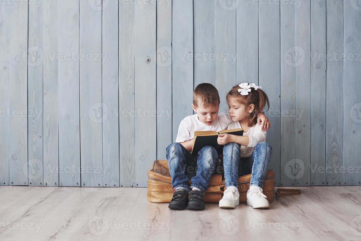 listo para grandes viajes. feliz niña y niño leyendo un libro interesante con un maletín grande. concepto de libertad e imaginación foto