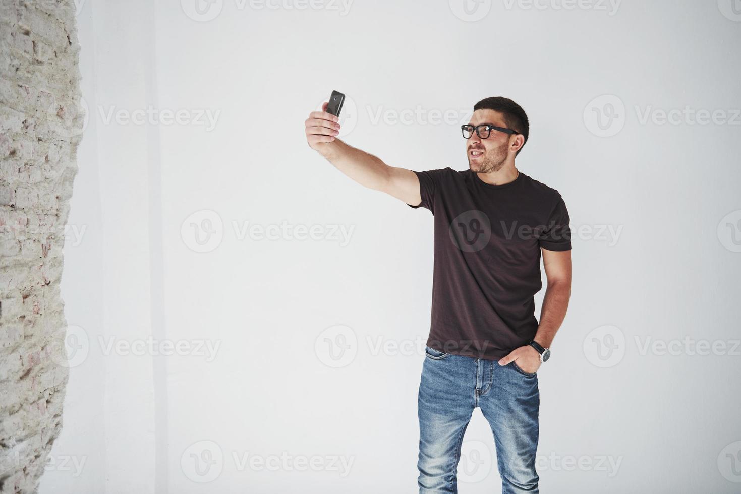 Playful bearded man making selfie on smartphone and white wall background photo