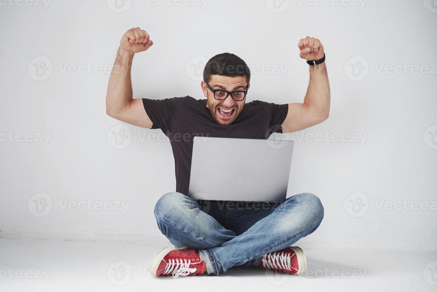 Young caucasian man sitting over white brick wall using computer laptop happy in shock with a surprise face, afraid and excited with fear expression photo