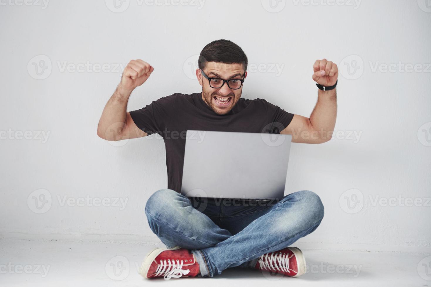 Young caucasian man sitting over white brick wall using computer laptop happy in shock with a surprise face, afraid and excited with fear expression photo