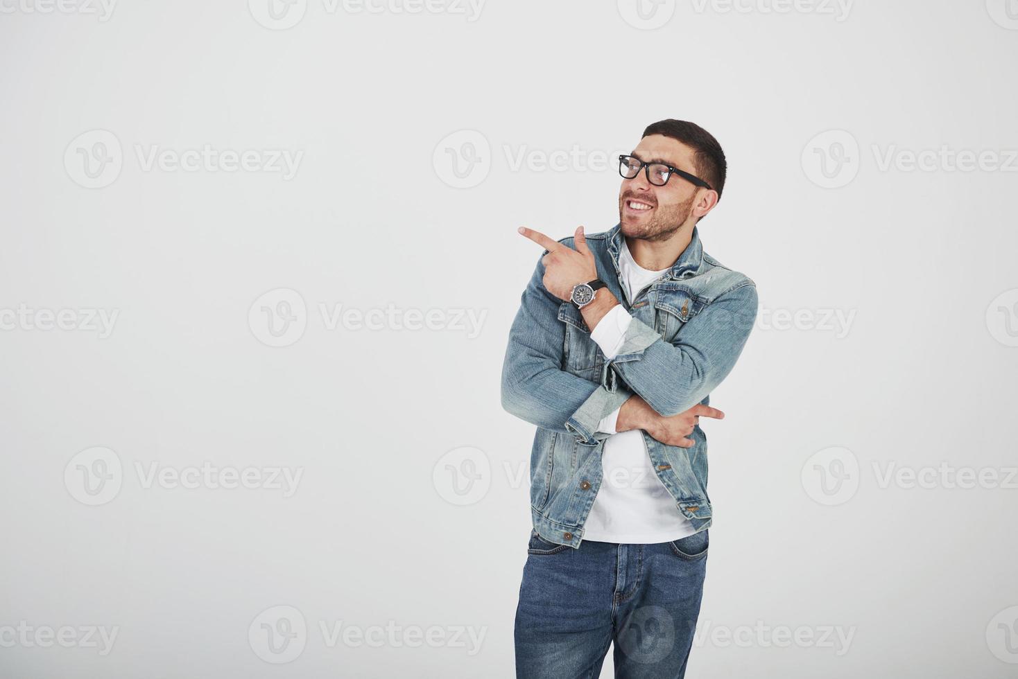 Feliz emocionado hombre barbudo en anteojos mirando a la cámara con una sonrisa y apuntando hacia el espacio de la copia con dos dedos aislado sobre fondo blanco. foto