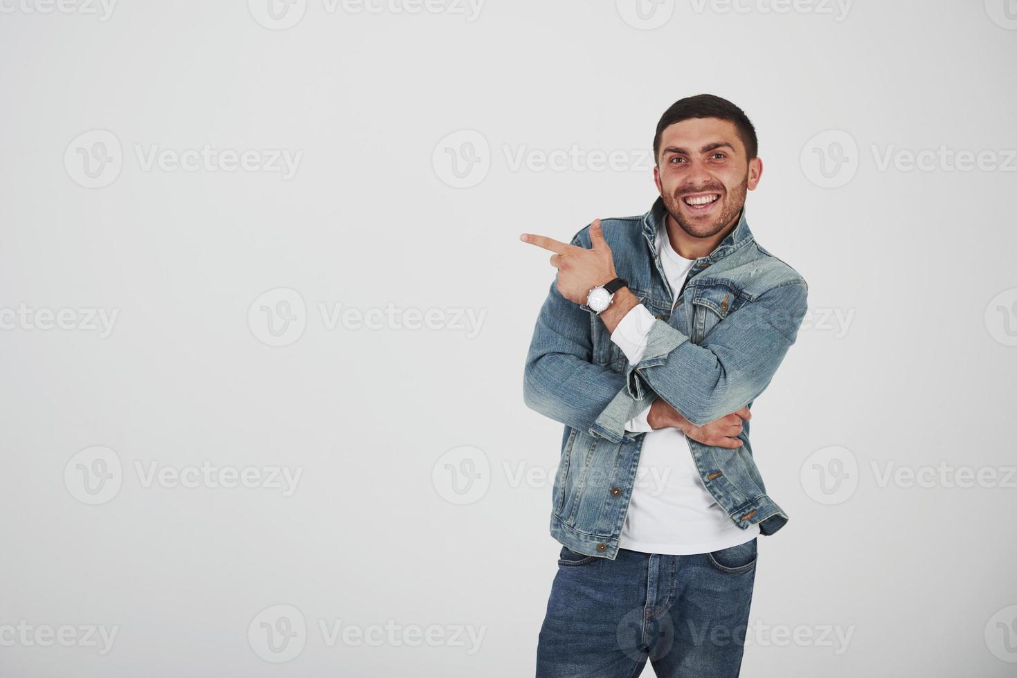 Feliz emocionado hombre barbudo en anteojos mirando a la cámara con una sonrisa y apuntando hacia el espacio de la copia con dos dedos aislado sobre fondo blanco. foto