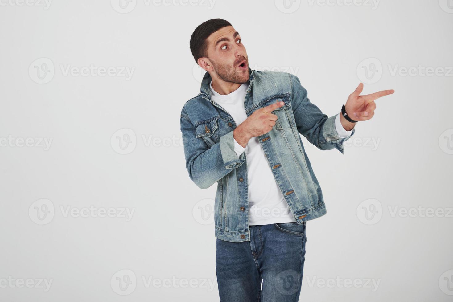 Happy excited bearded man in eyeglasses looking at camera with smile and pointing away at copy space with two fingers isolated over white background photo