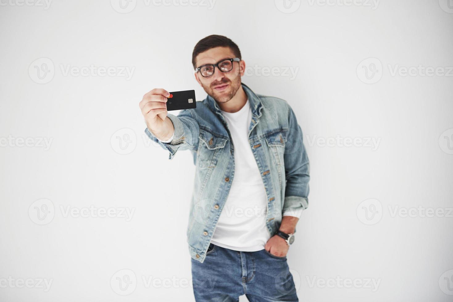 Ejecutivo de negocios masculino guapo joven en traje casual sosteniendo una tarjeta de crédito en los bolsillos sobre un fondo blanco. el concepto de comercio en Internet y la facilidad del dinero electrónico foto