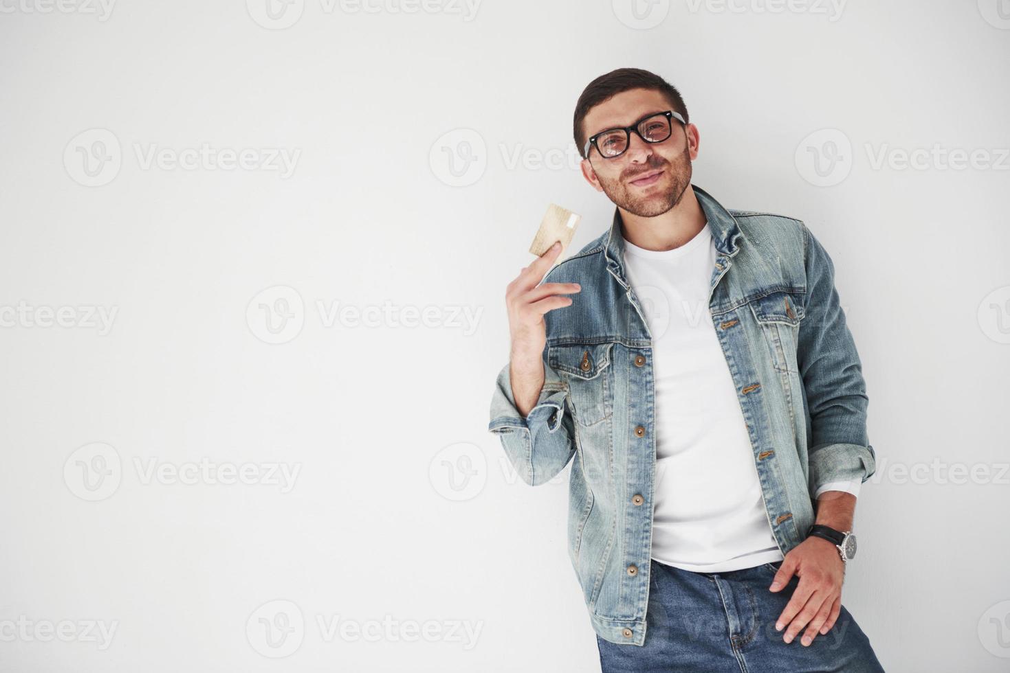 Ejecutivo de negocios masculino guapo joven en traje casual sosteniendo una tarjeta de crédito en los bolsillos sobre un fondo blanco. el concepto de comercio en Internet y la facilidad del dinero electrónico foto