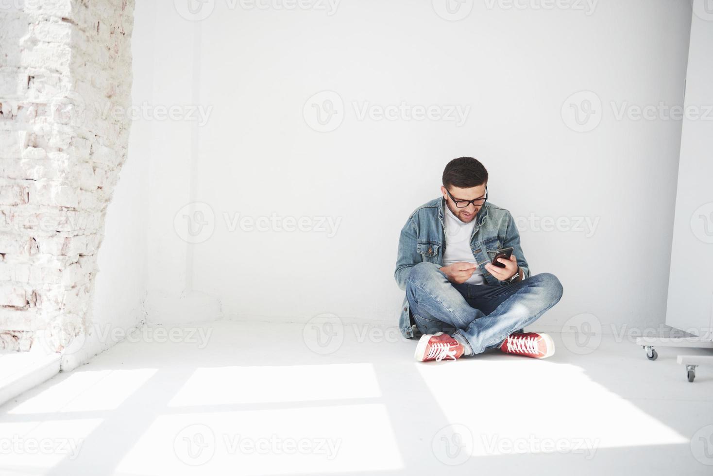 A guy in casual clothes is sitting at home in an empty apartment holding a credit card and calling on the phone. Maybe he's a new resident and has not bought any furniture yet. photo