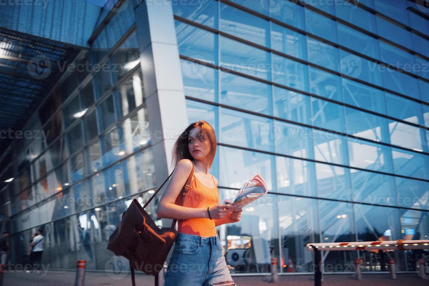 una hermosa joven con una mochila detrás de los hombros de pie en la calle cerca de un aeropuerto. ella acaba de llegar del resto y muy feliz foto