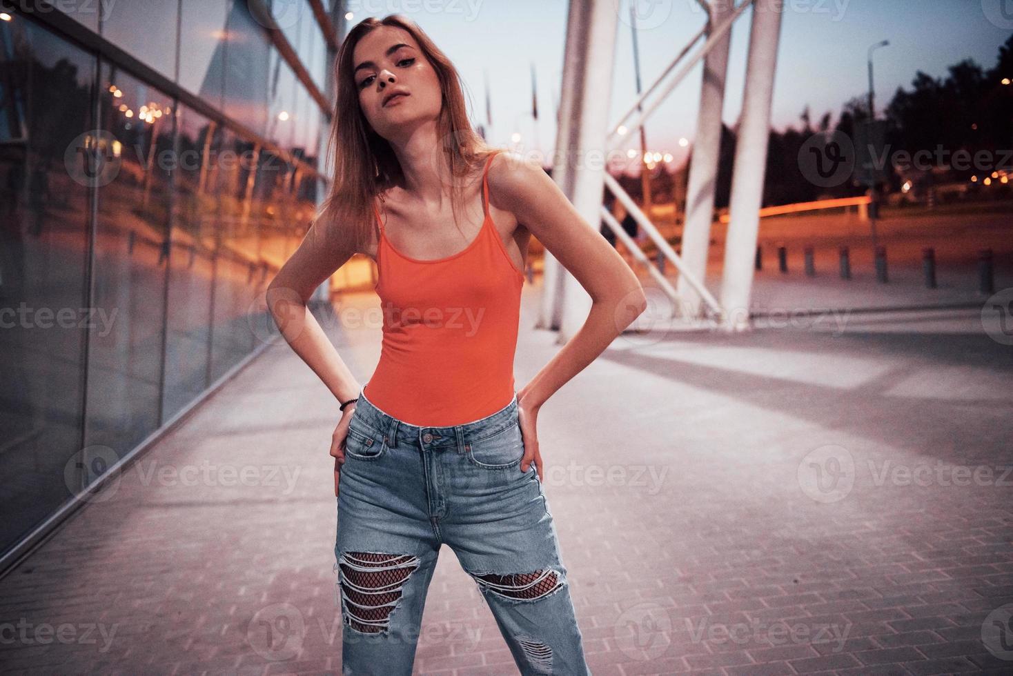 Beautiful sexy tourist girl walking in busy city street near the airport. Woman looking at camera outdoors wearing fashionable red t-shirt photo