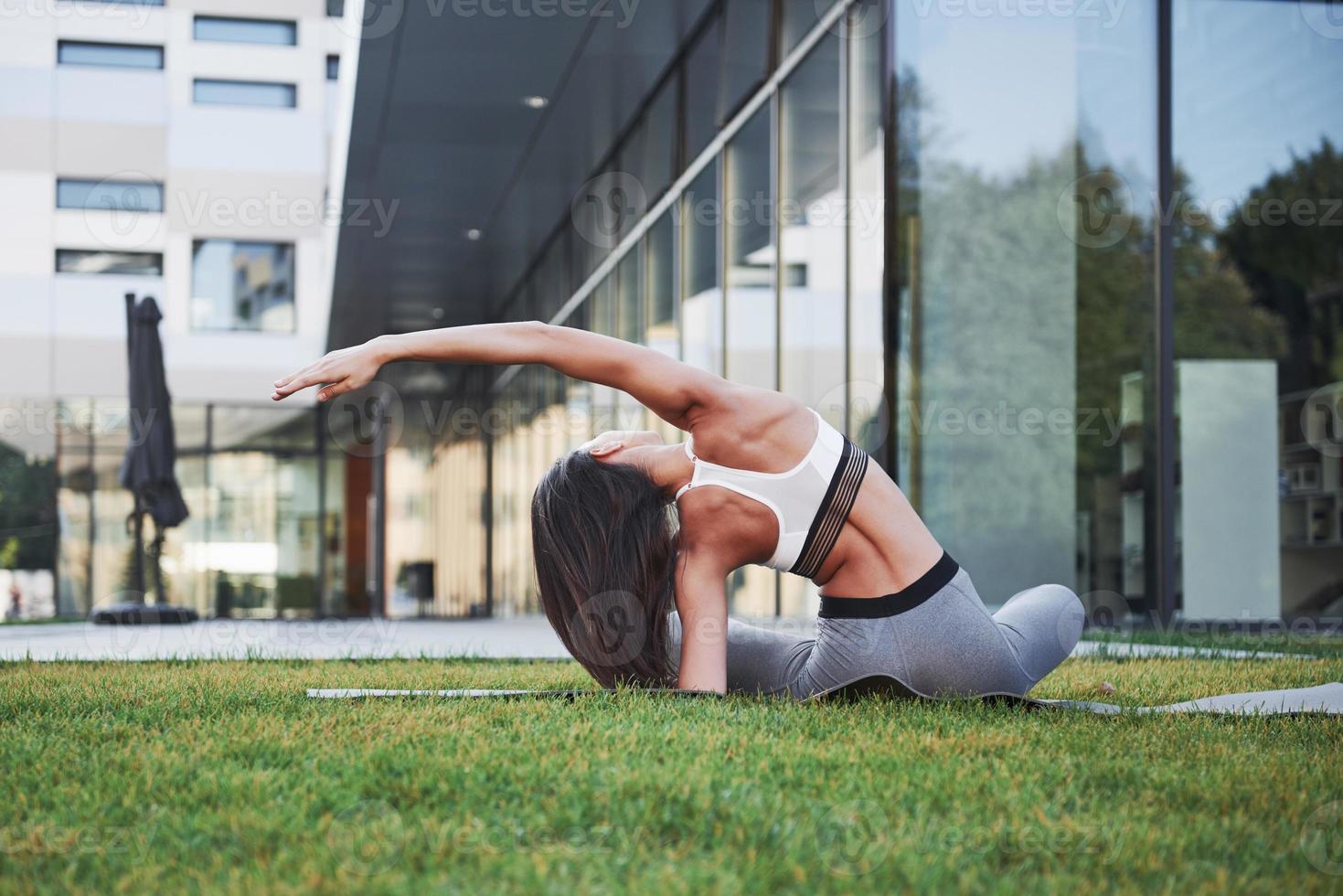 Sunny summer morning. Young athletic woman doing handstand on city park street among modern urban buildings. Exercise outdoors healthy lifestyle photo