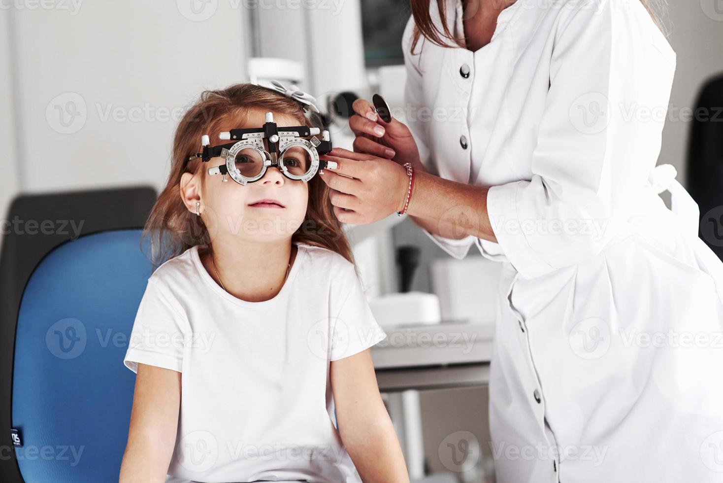 buscar. doctor revisando la vista de la niña y ajustando el foróptero foto