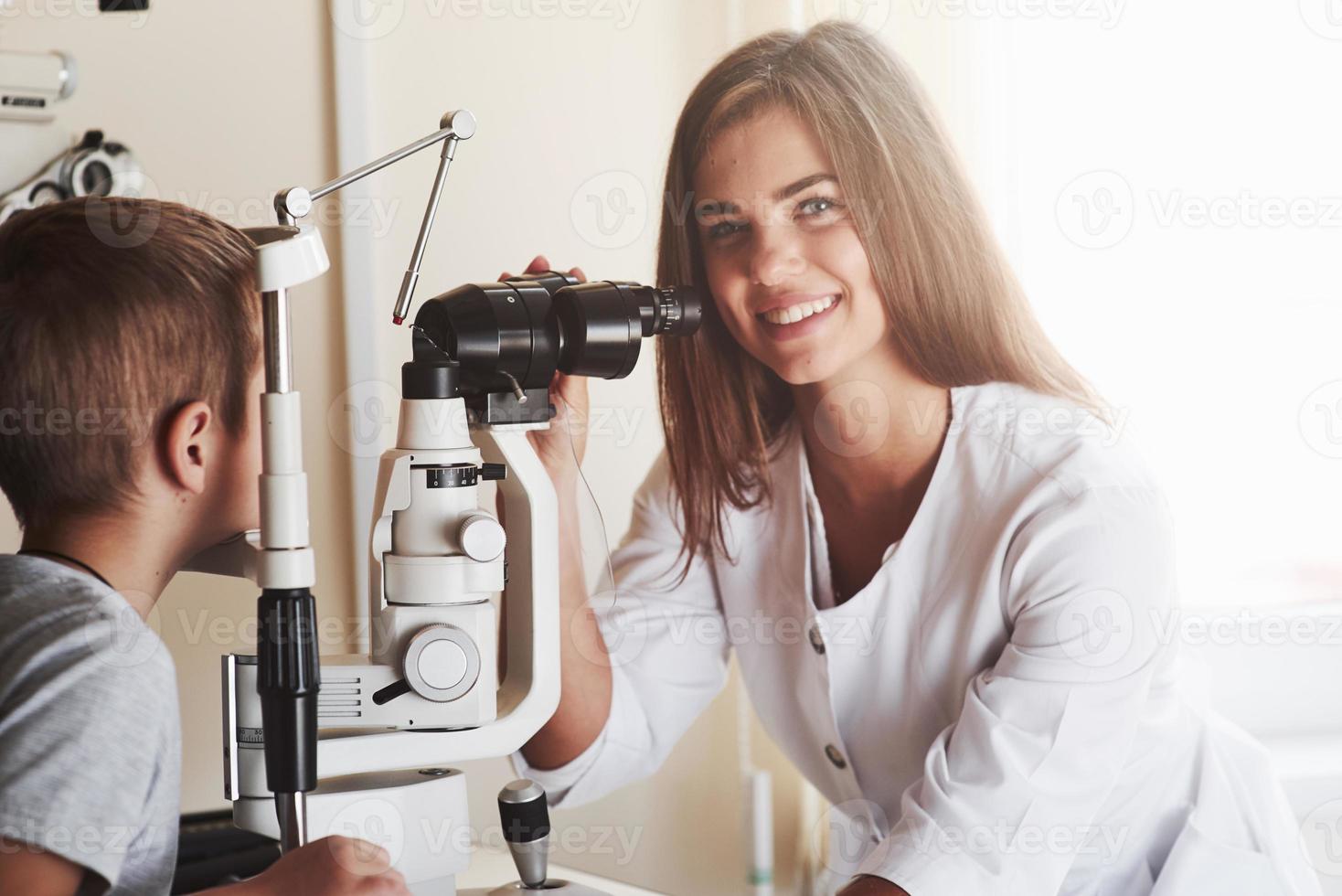 mujer hermosa. El niño pequeño tiene una prueba para sus ojos con un aparato óptico especial por una doctora. foto