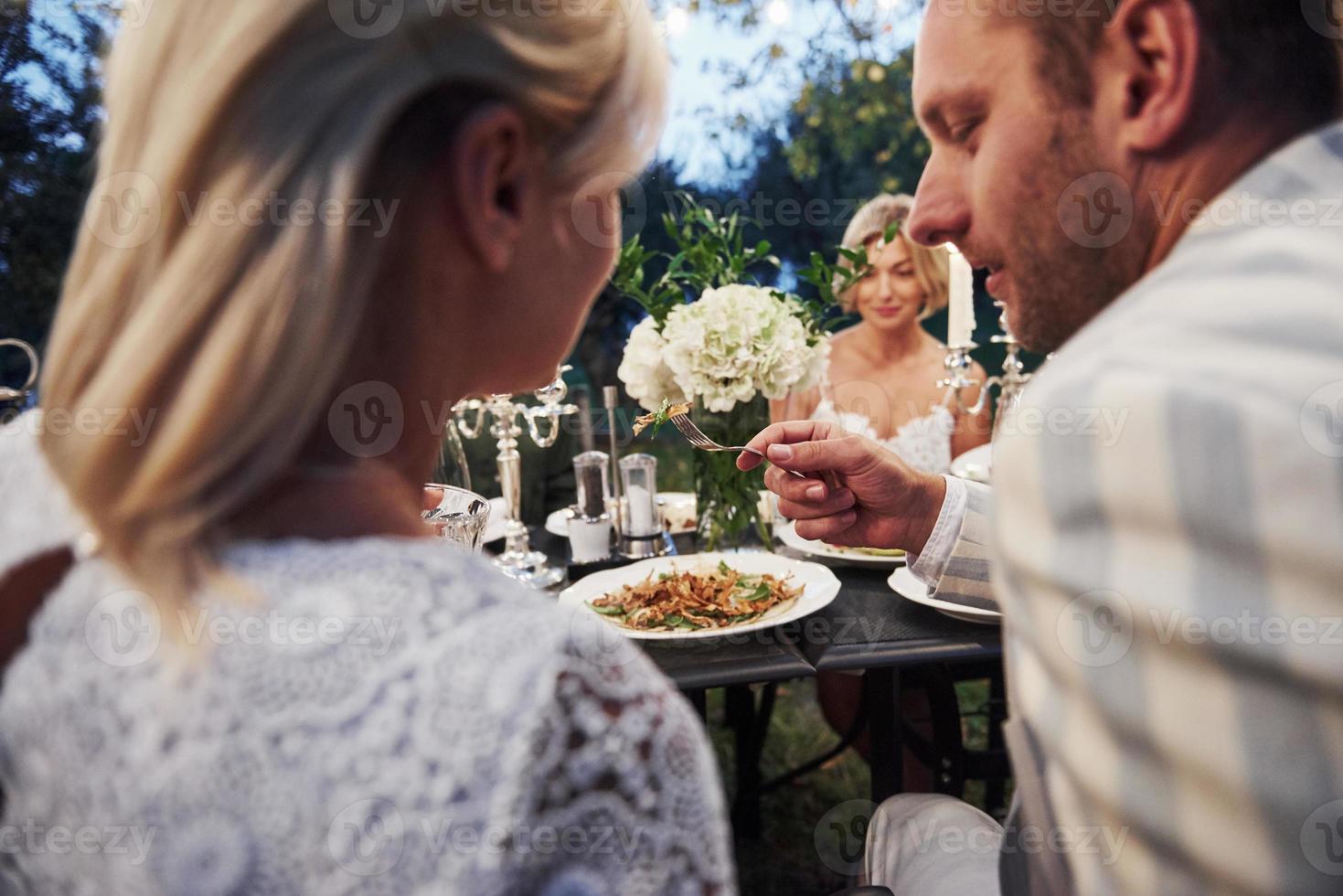 el hombre le da ensalada a su esposa para que la pruebe. Los amigos se reúnen por la noche. bonito restaurante exterior foto