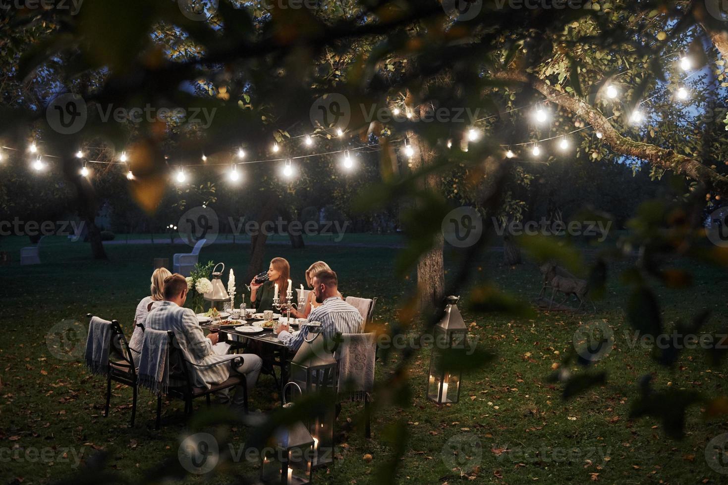 Photo through tree branches with leaves. Evening time. Friends have a dinner in the gorgeous outdoor place