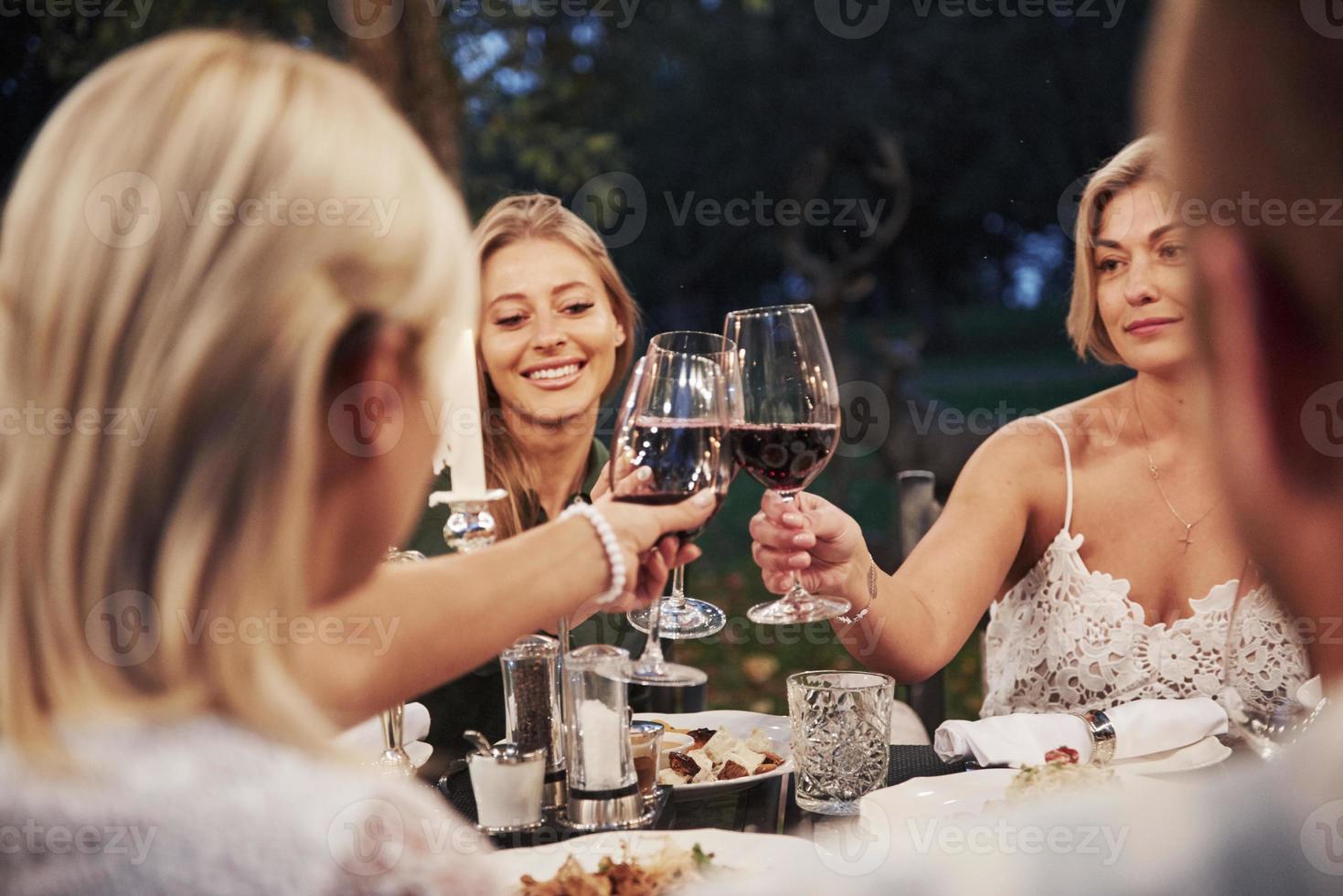 mujeres rubias con copas de vino. grupo de amigos con ropa elegante tienen una cena de lujo foto