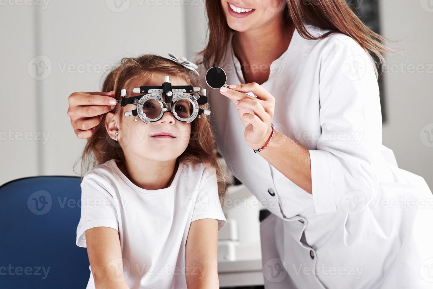 cuando el trabajo te da una sonrisa. doctor revisando la vista de la niña y ajustando el foróptero foto