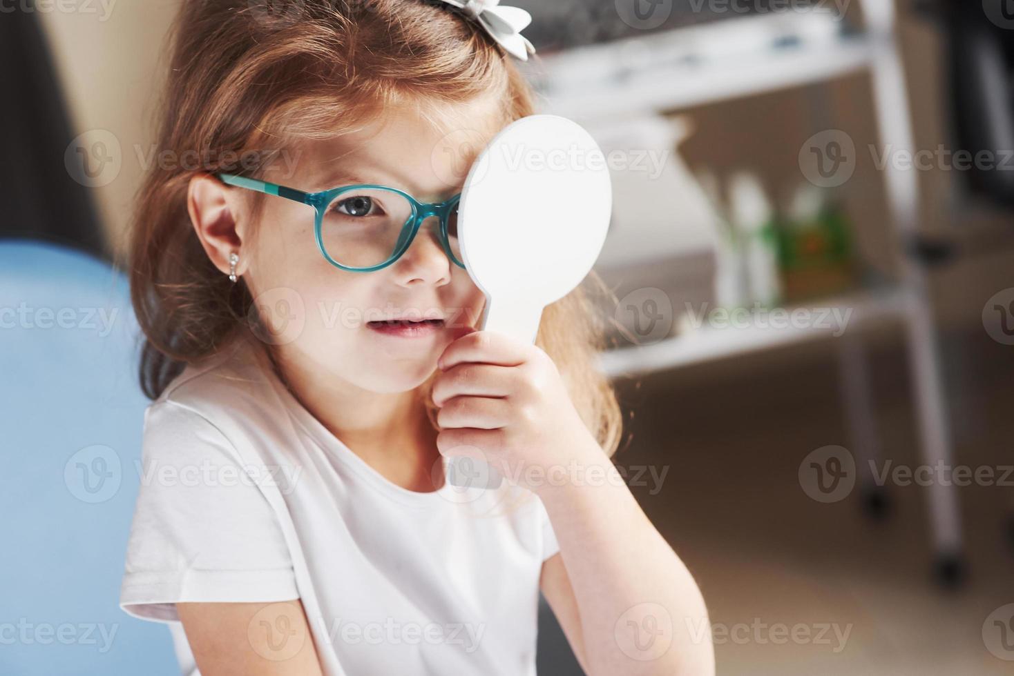 Holds by herself the occluder. Little girl checking his vision with new green glasses photo