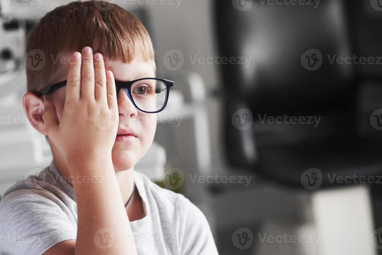 vista frontal. cierre el ojo derecho con la mano. niño comprobando su visión con gafas negras nuevas foto