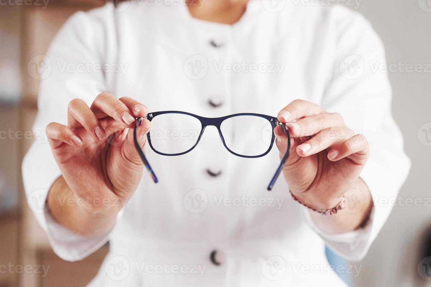 vista frontal. manos de mujer sostiene los anteojos azules en el gabinete del médico foto