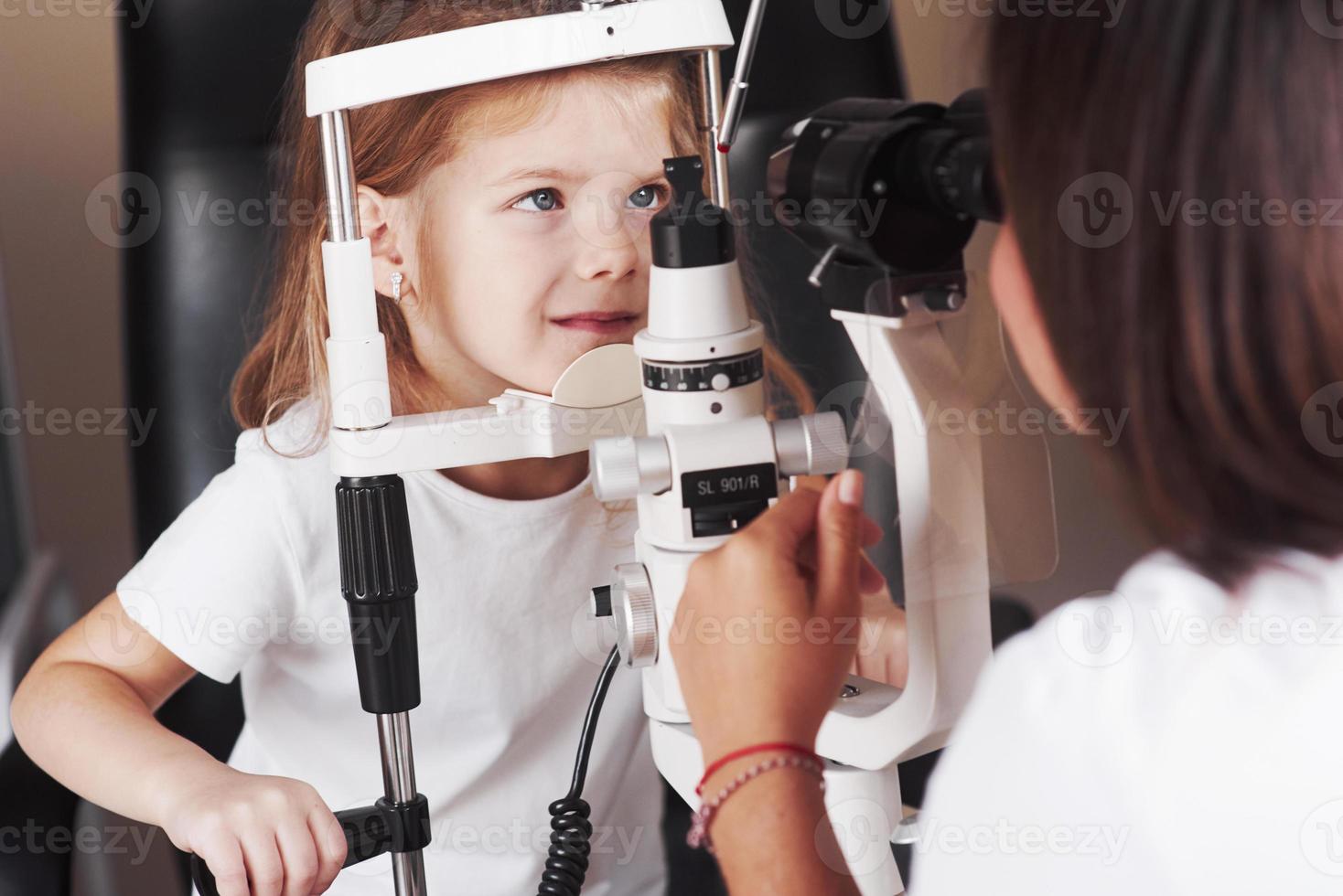 mirar de frente. La niña tiene una prueba para sus ojos con un aparato óptico especial por una doctora. foto