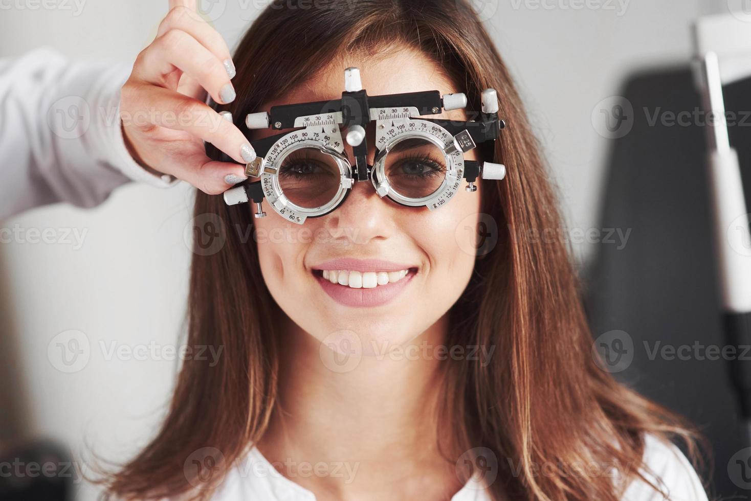 Atractiva chica sonriendo mientras usa foróptero que sintonice el médico foto