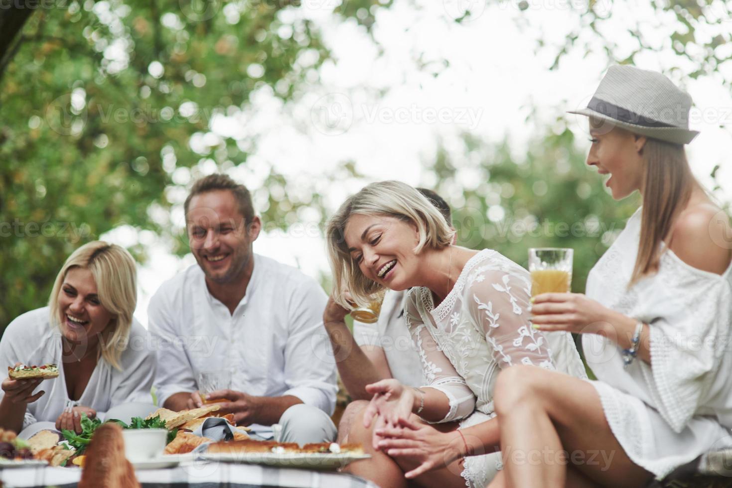 Good friends sit outdoors near the table with food, have dinner and laughing photo