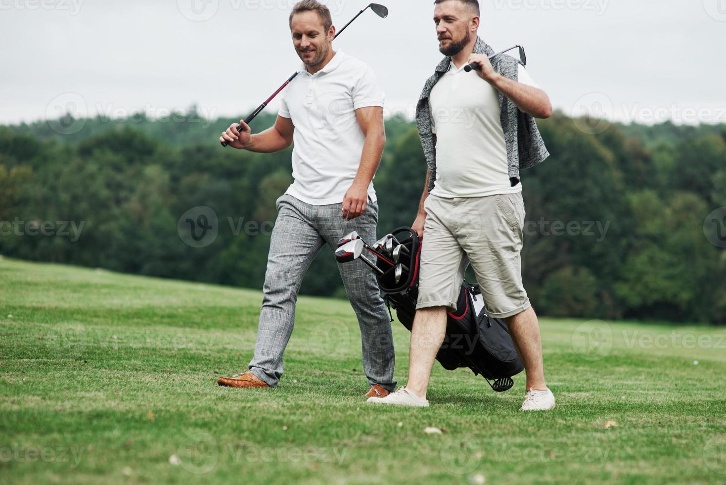 dos amigos caminando por el césped con equipo de golf y hablando foto