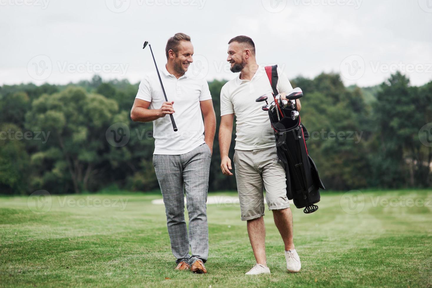 Having good time. Two friends walking through the lawn with golf equipment and talking photo