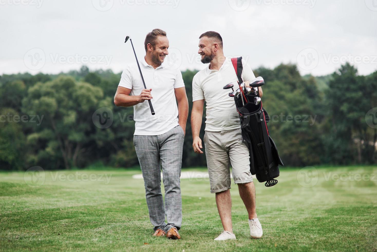 pasarlo bien. dos amigos caminando por el césped con equipo de golf y hablando foto