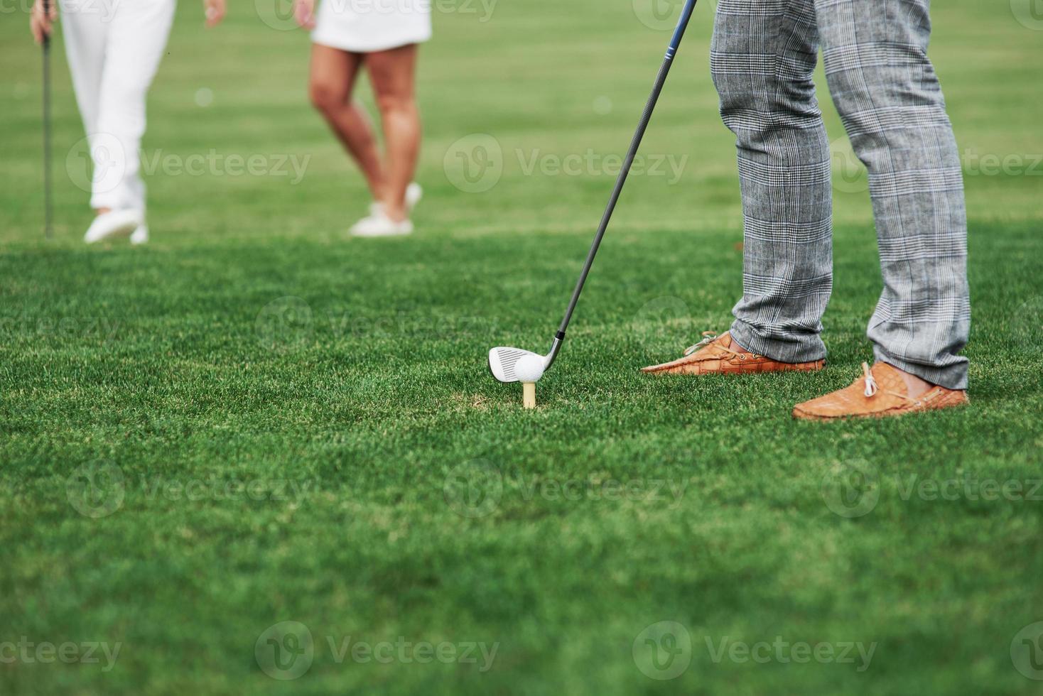 Cropped image of golfer who take aim for the shot. Two friends standing at background photo
