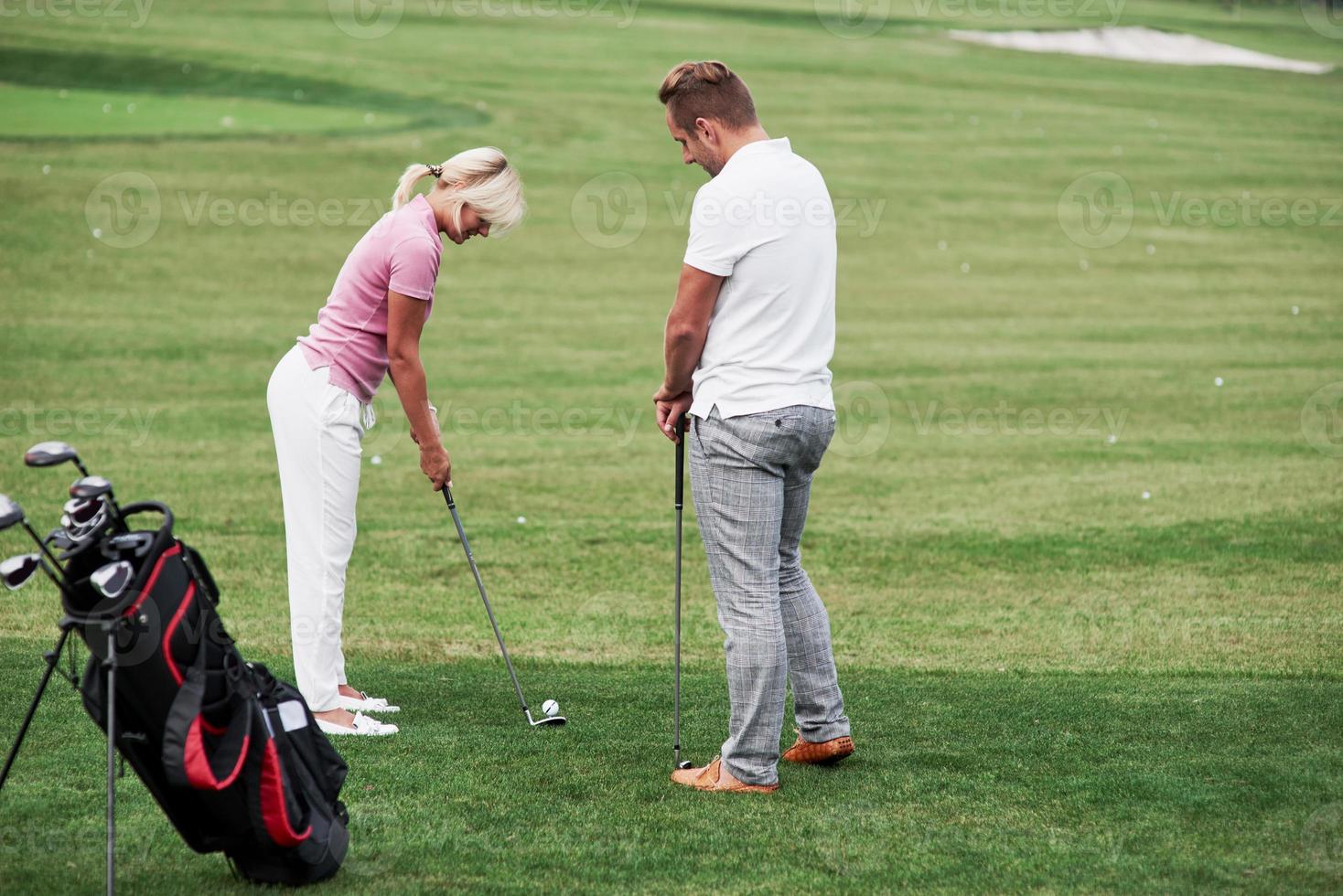 Adult man teaching the woman how to play the golf on the field with green grass photo