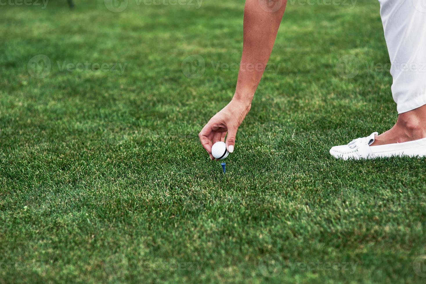 Female hand putting golf ball on the pin standing in the green field photo