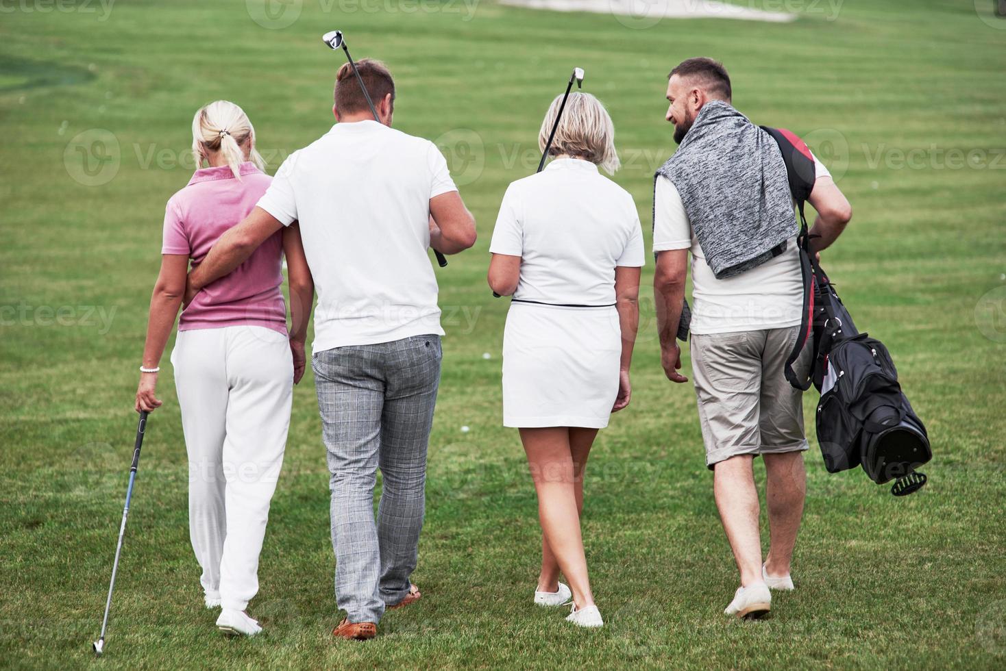 amigos caminando por el campo de deportes con palos de golf y divirtiéndose el fin de semana foto