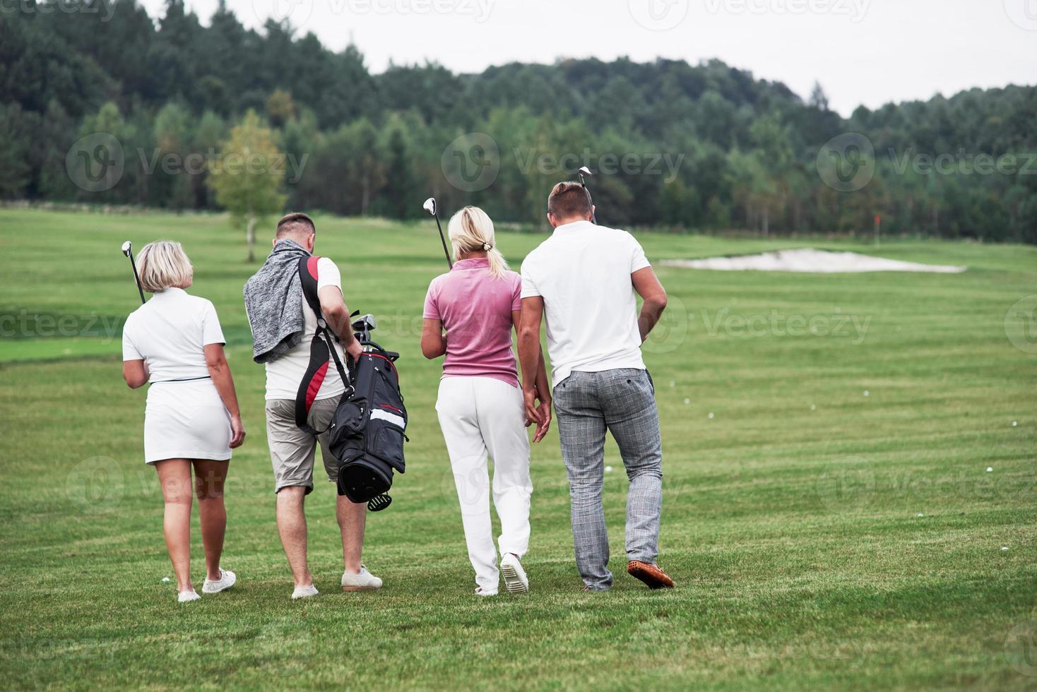 Group of four friends carying golf equipment going to the next point of the field photo