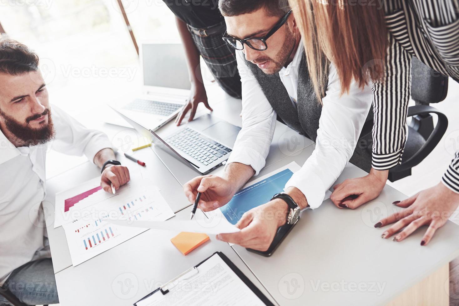 Cuatro empleados multirraciales tienen trabajo en la oficina usando la computadora portátil en la mesa foto