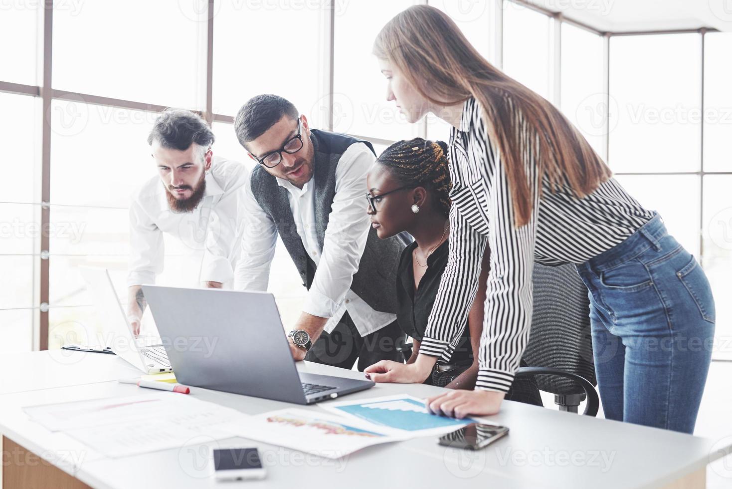 gerente en las gafas hablar sobre el plan. Cuatro empleados multirraciales tienen trabajo en la oficina usando la computadora portátil en la mesa foto