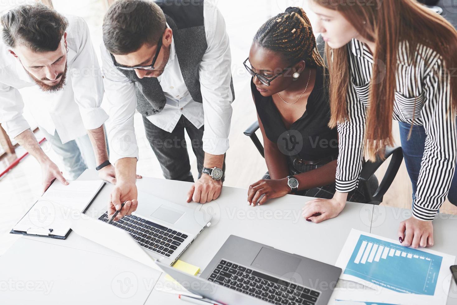 Photo from the top. Four multiracial employee have work in the office using the laptop on table