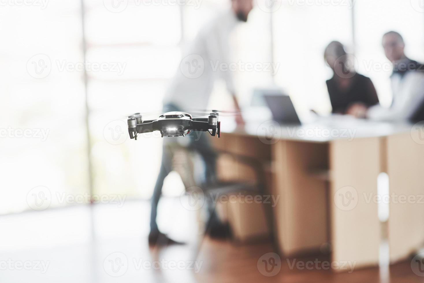 Flying drone is in the office room. Employees sitting and watching for it at background photo