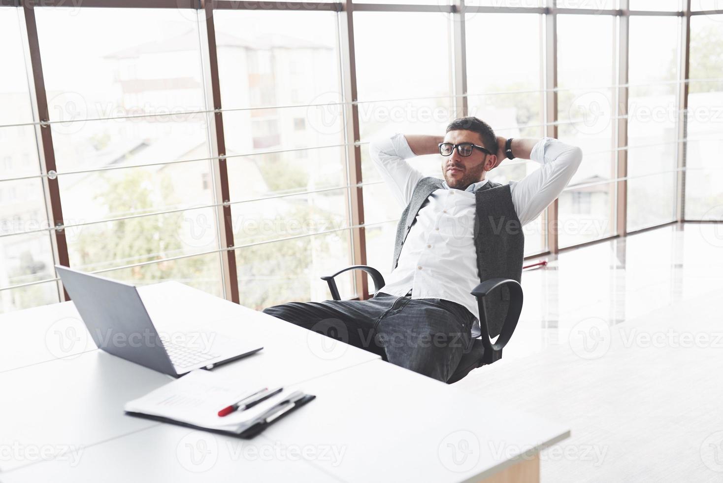 Young businessman having a rest while sitting in chair in the clean room and watching to the laptop photo