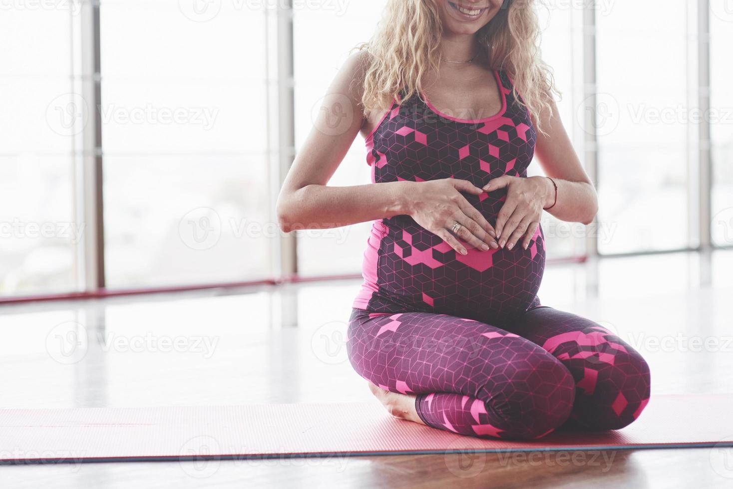 Young pregnant woman sitting in the hall and keeps hands on her belly to create shape of the heart photo
