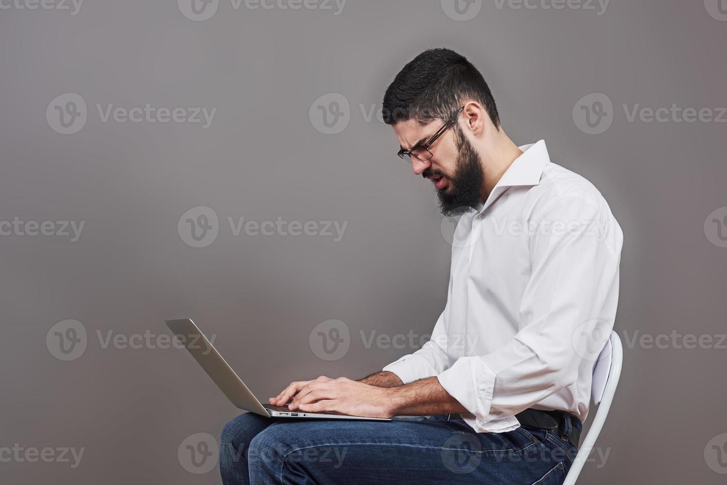 Handsome business man in glasses and suit holding laptop in hands and writing something. Side view. Isolated gray background photo