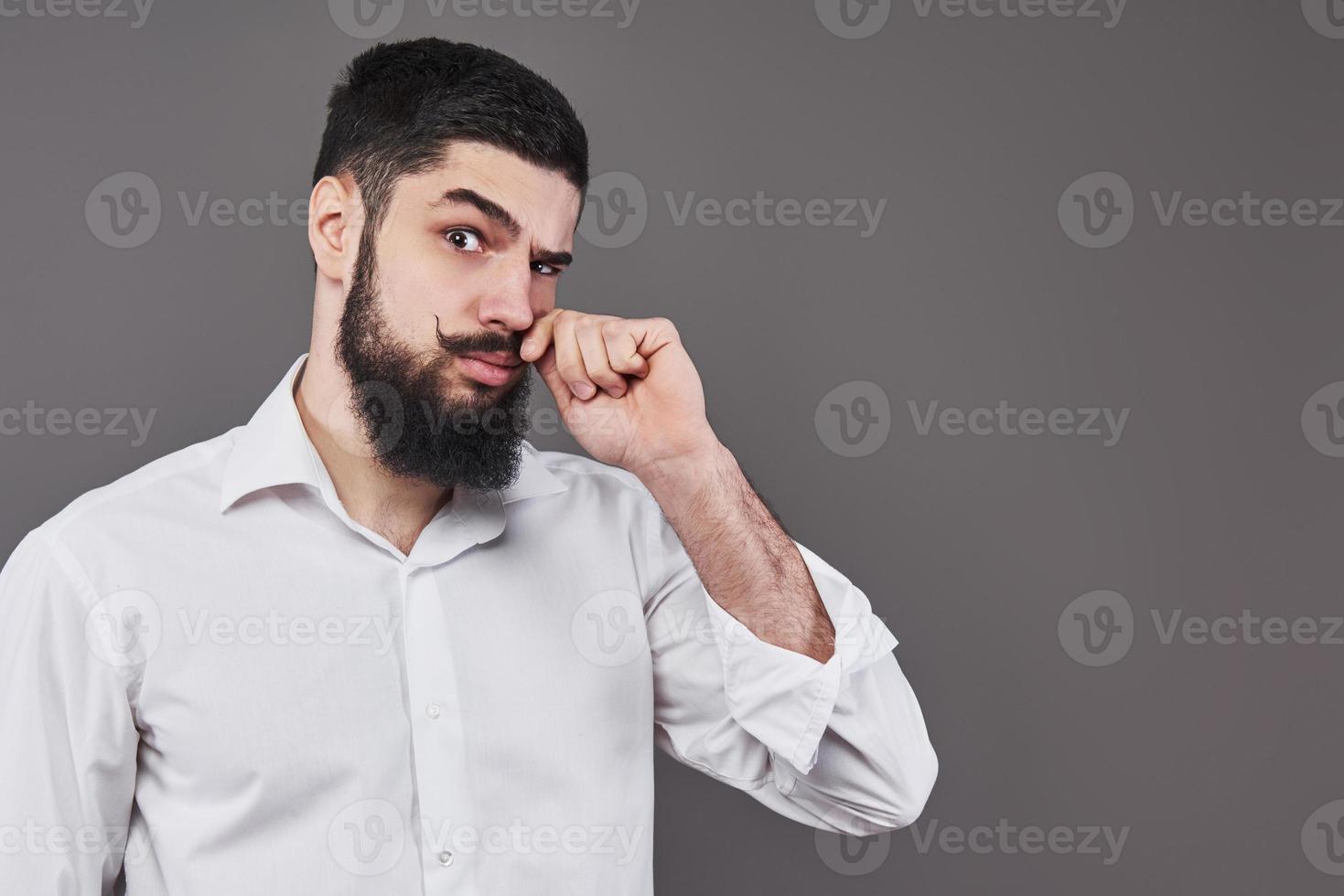 hipster con cara seria. sentimiento y emociones. chico o hombre barbudo sobre fondo gris. peluquería de moda y belleza. hombre con barba larga y bigote, espacio de copia foto