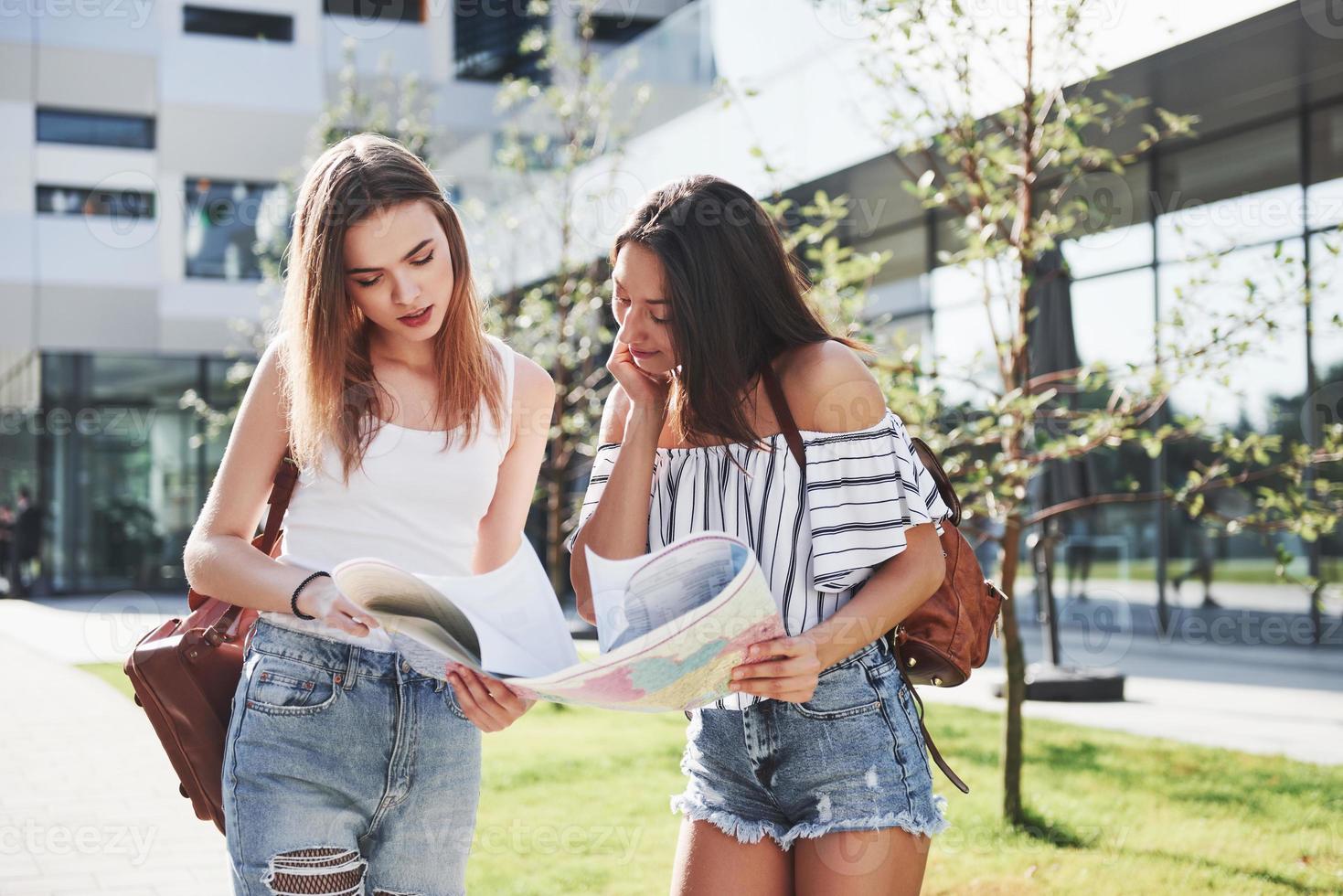 chicas jóvenes que leen el mapa de la ciudad y buscan hotel. turistas encantadores con mochilas determinan el concepto de conocimiento del mundo foto