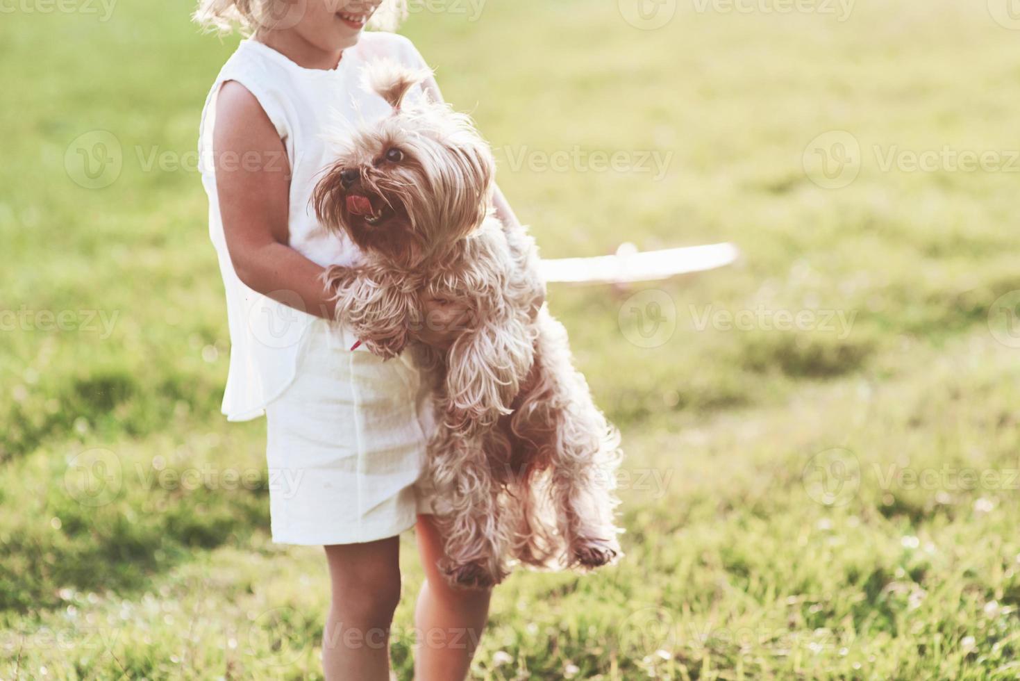 activo y alegre. Sonriente niña alegre sosteniendo perrito y jugando con él afuera en el campo foto