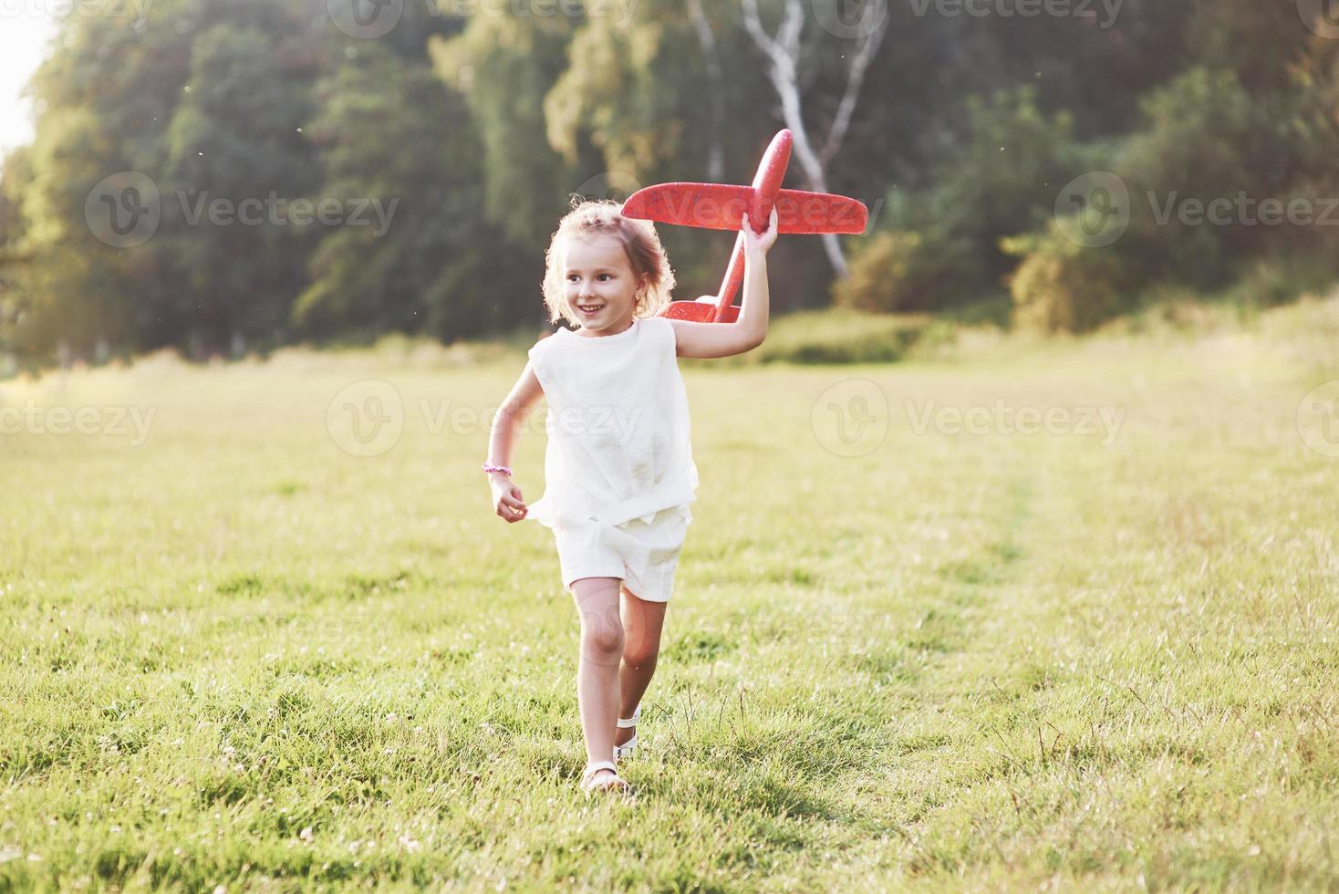 Sincere emotions. Happy little girl running on the field with red toy plane in their hands. Trees at background photo