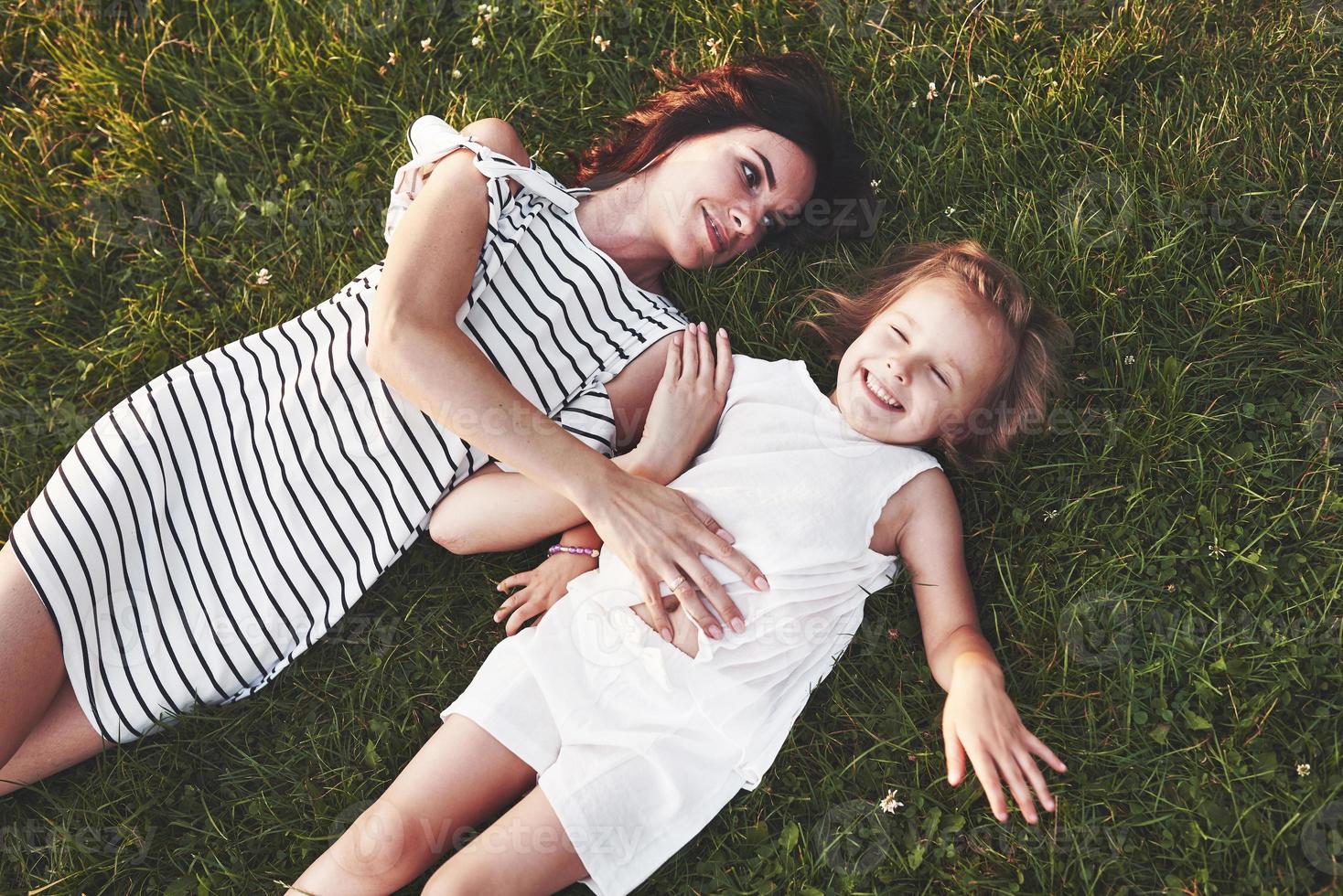 Someone is scared of tickling. Top view of children and mother laying down on the grass filled with sunshine and looking at each other photo