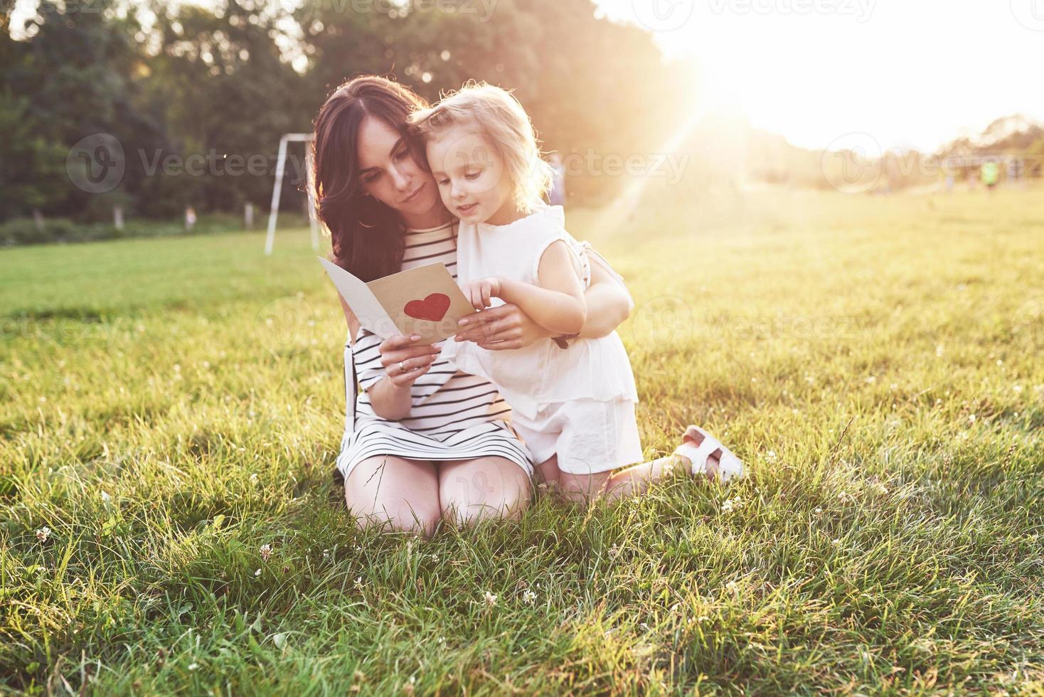 Sunlights from above. Mother and daughter sitting and reading the little book with heart on it's cover photo