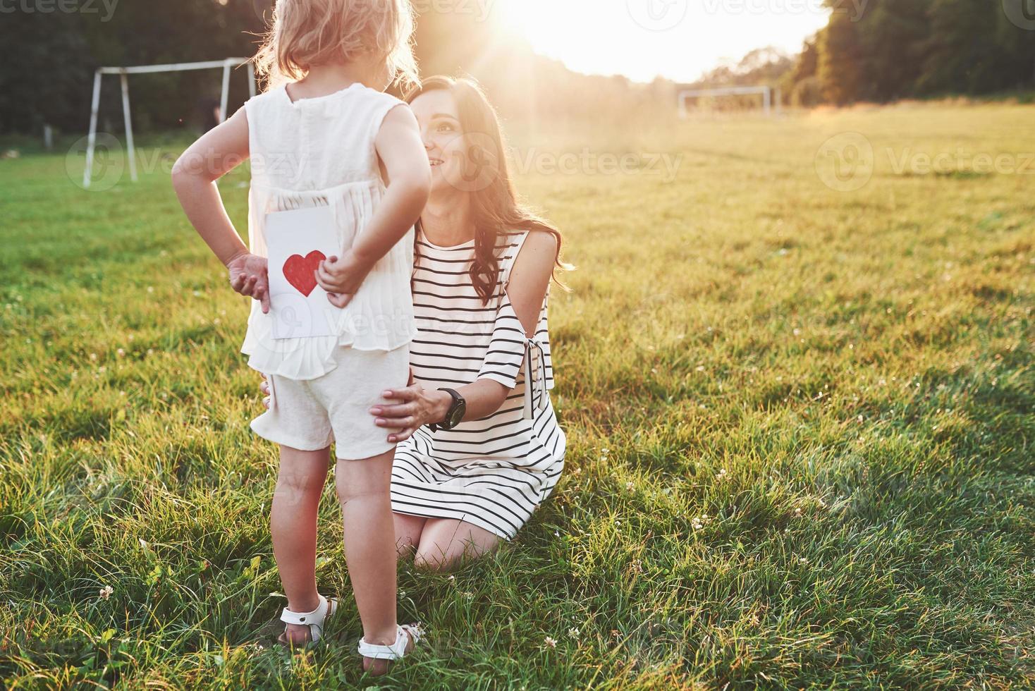 niña esconde el libro con corazón rojo en la parte posterior de la madre sentada sonriente foto