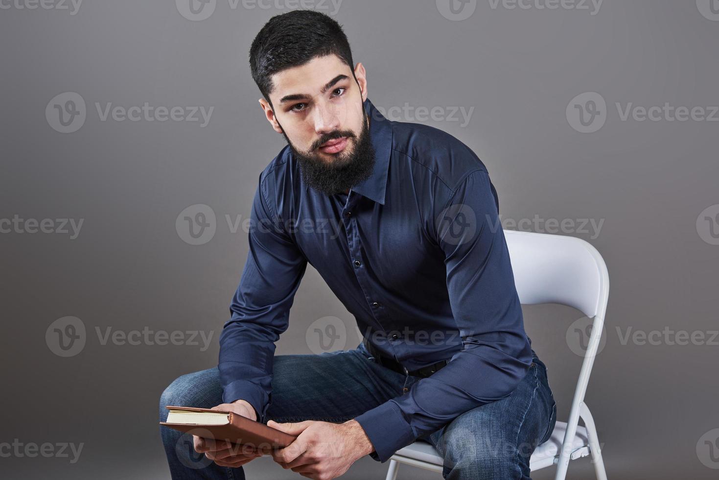 Portrait of toothy handsome bearded man sitting on a chair with book on hands photo