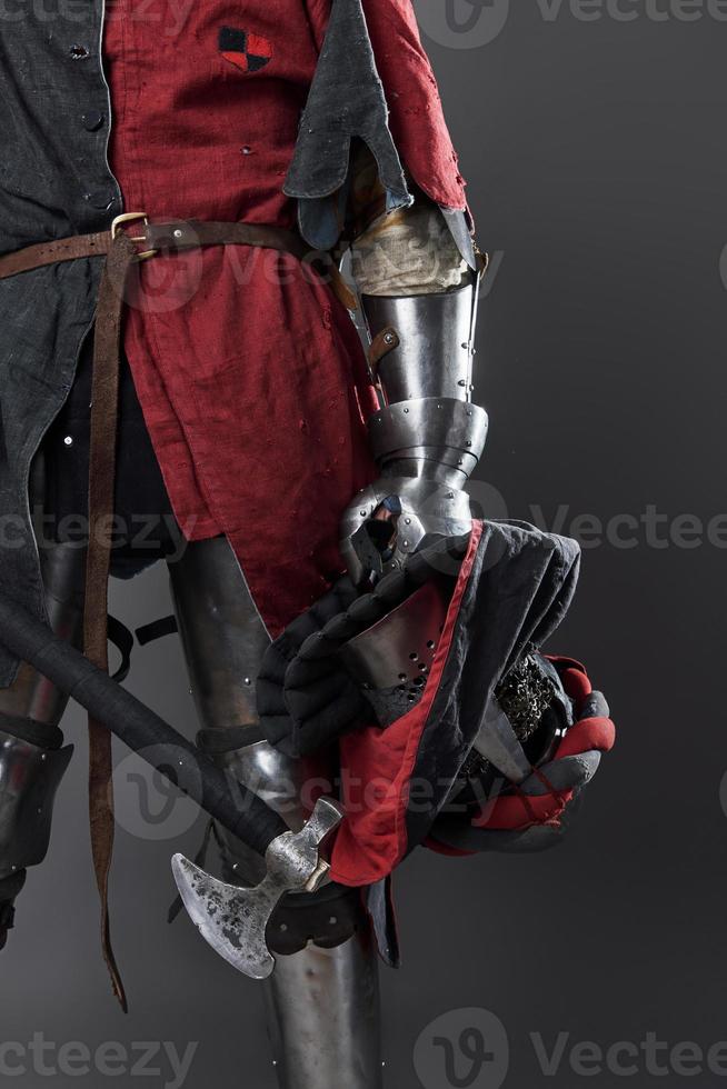 Medieval knight on grey background. Portrait of brutal dirty face warrior with chain mail armour red and black clothes and battle axe photo